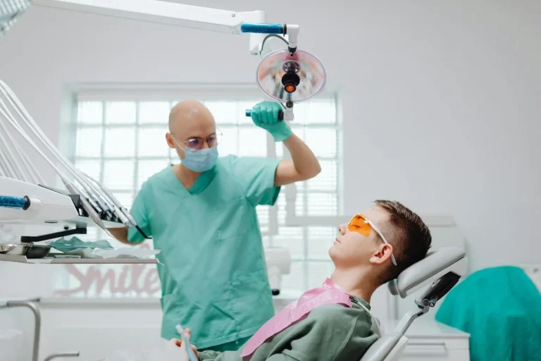 pacient pe scaunul medical si stomatologul langa, cu mana pe lampa